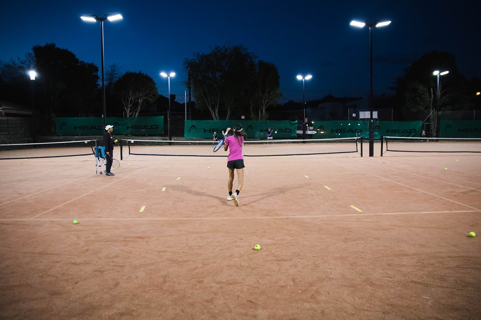 Players under lights on the clay courts at dusk
