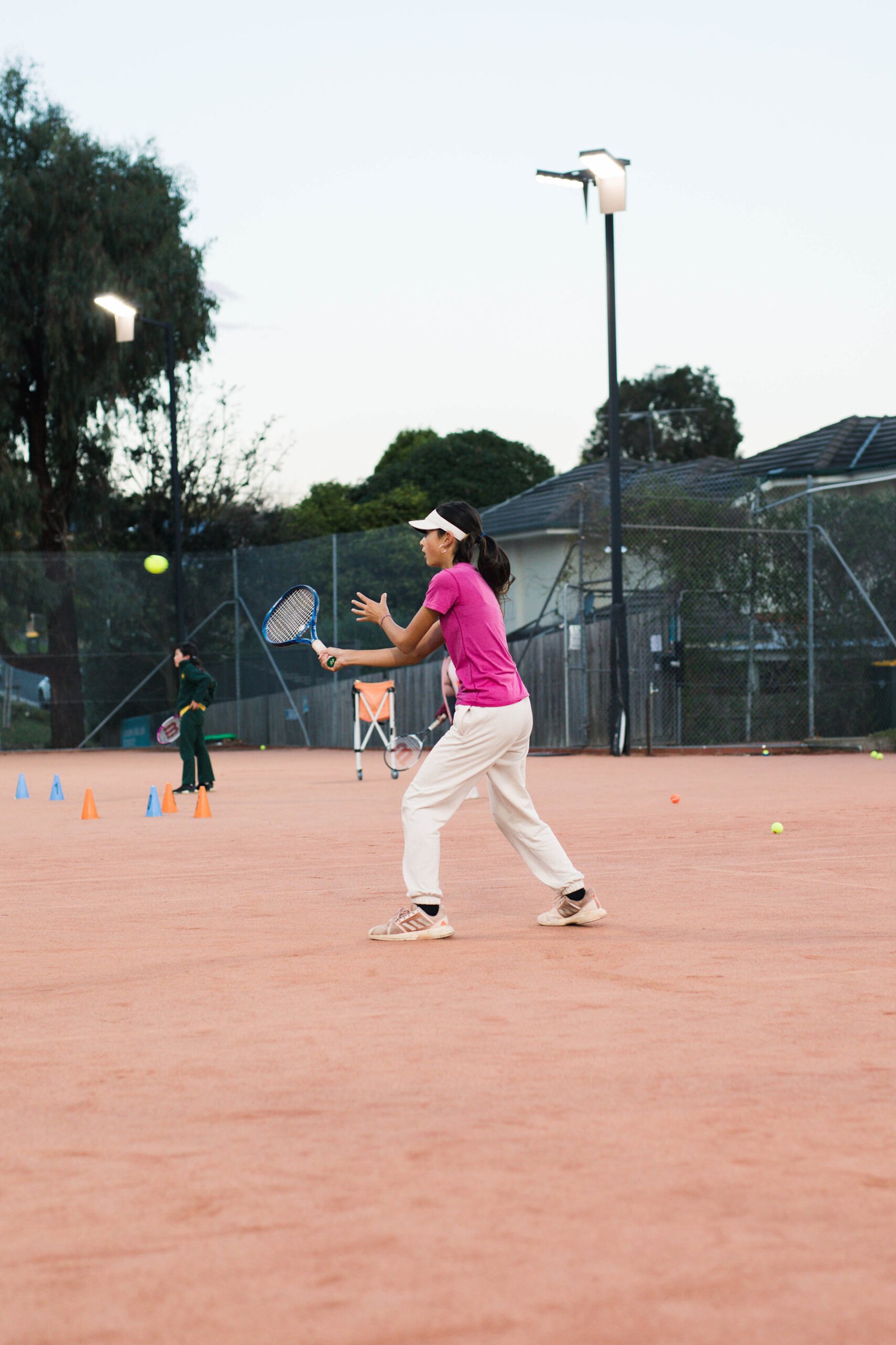 A junior player setting up a forehand on the clay at dusk